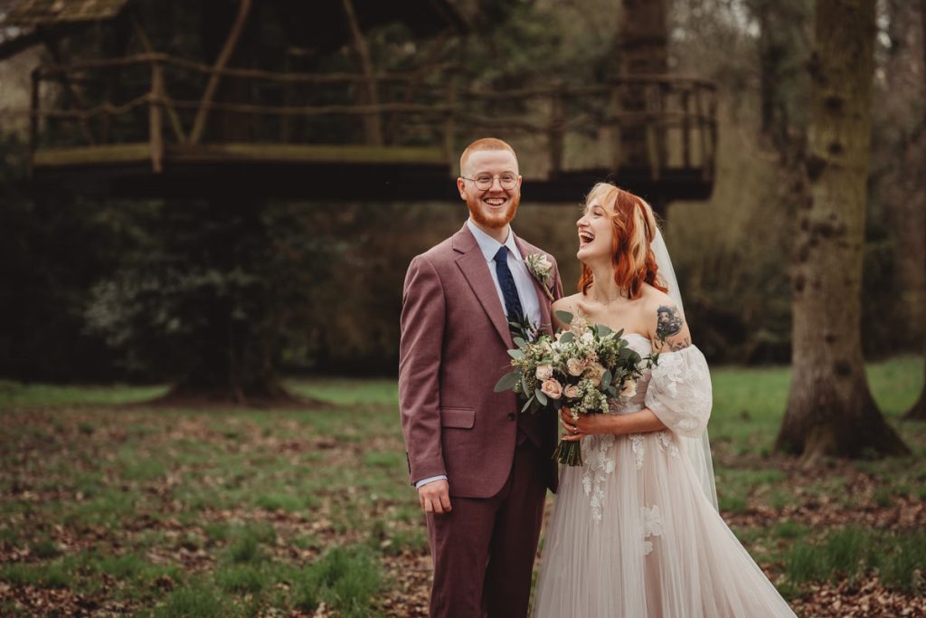 Bride and groom laughing outdoors in forest setting.