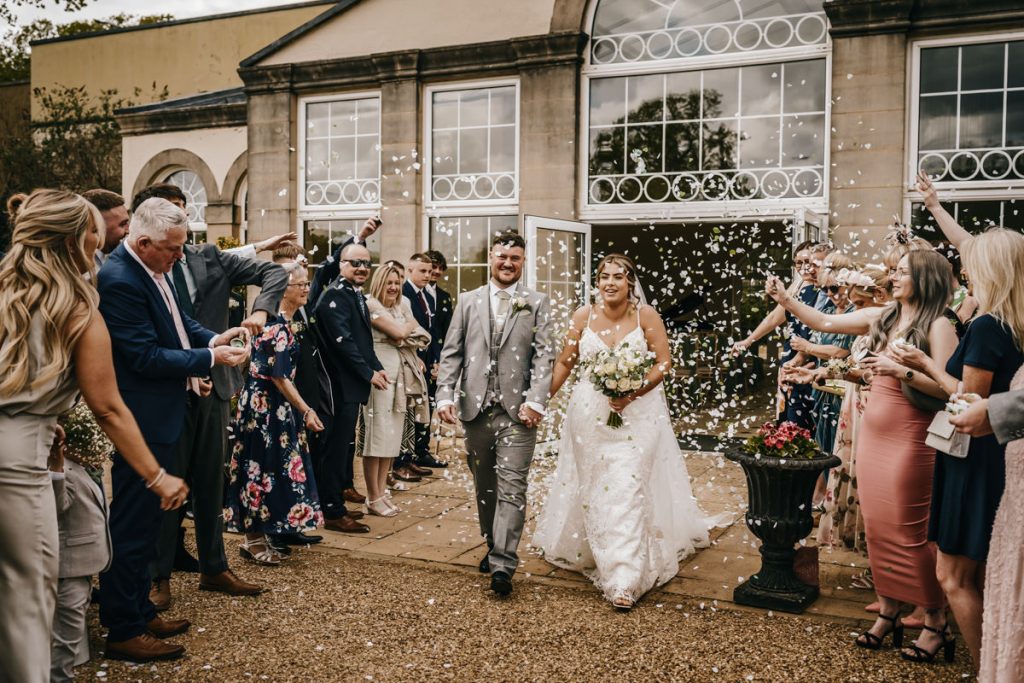 Bride and groom exit wedding, showered with confetti at Whittlebury Park