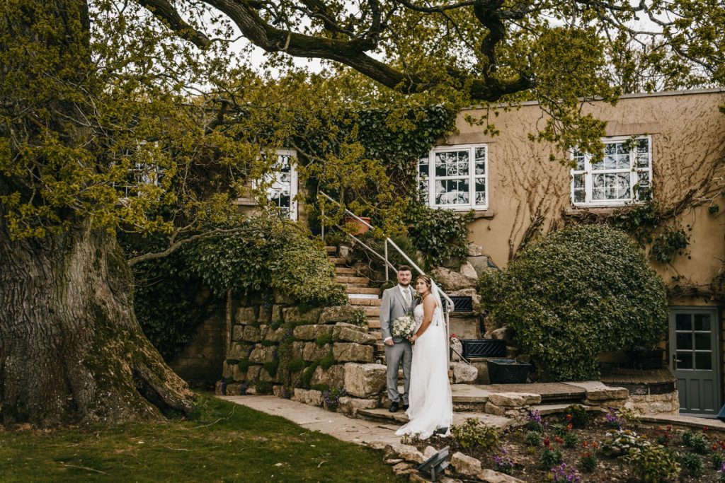 Bride and groom outdoors by ivy-covered building at Whittlebury Park