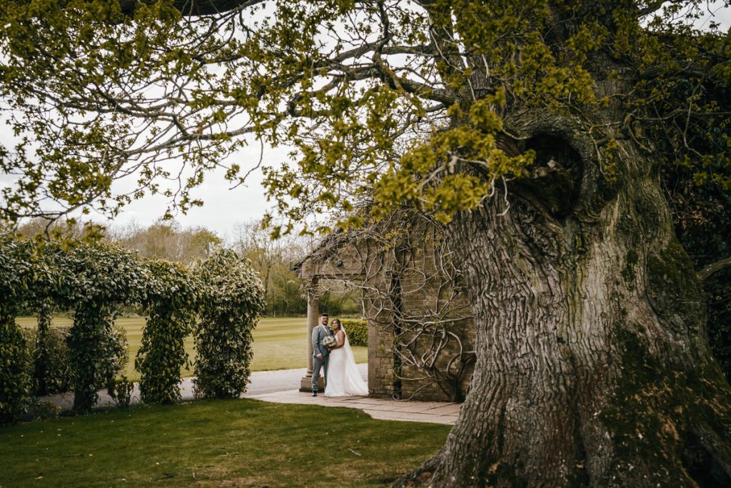 Bride and groom under large tree in garden at Whittlebury Park
