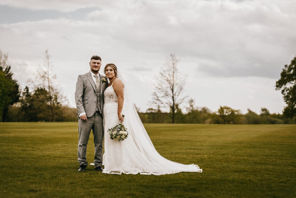 Bride and groom standing on green lawn at Whittlebury Park