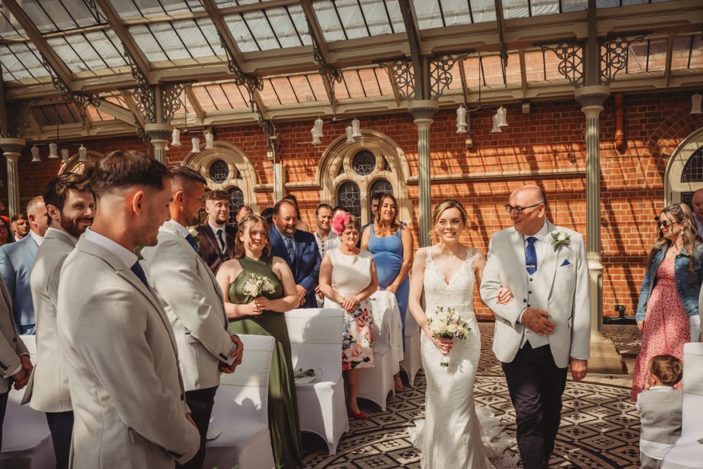 Bride walking down sunlit aisle with father at Kilworth House Hotel
