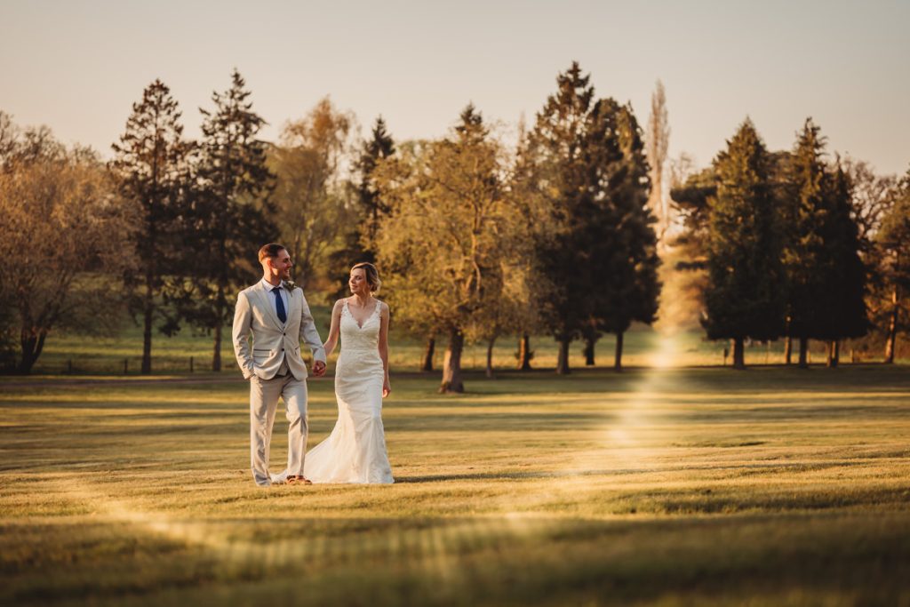 Bride and groom walk in sunny park at Kilworth House Hotel