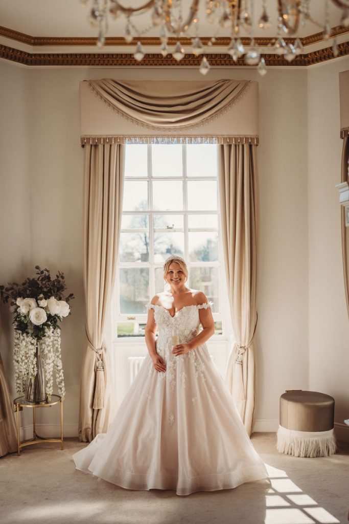 Bride in wedding dress by window in elegant room at Bourton Hall by Tom Stenlake Photography