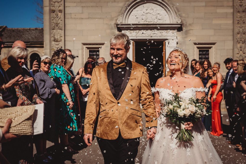Happy couple exits wedding amid confetti celebration at Bourton Hall by Tom Stenlake Photography