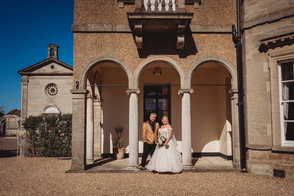 Couple posing outside historic building in sunlight at Bourton Hall by Tom Stenlake Photography