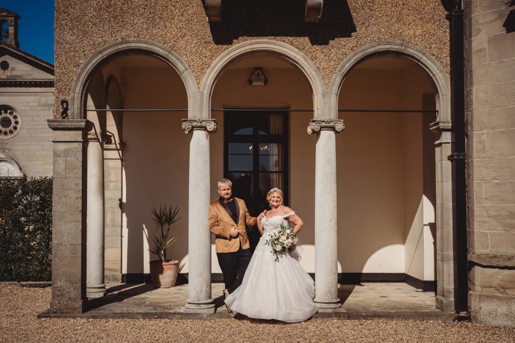 Couple in wedding attire under stone archway at Bourton Hall by Tom Stenlake Photography