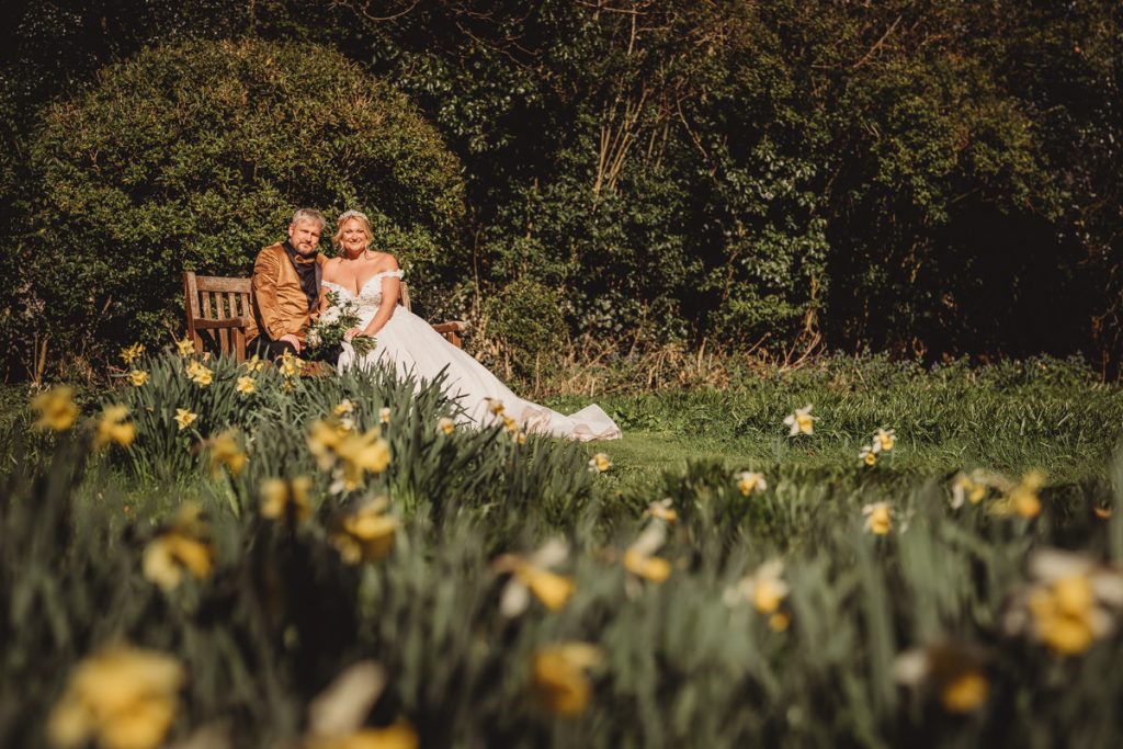 Couple sitting on bench in garden with flowers at Bourton Hall by Tom Stenlake Photography