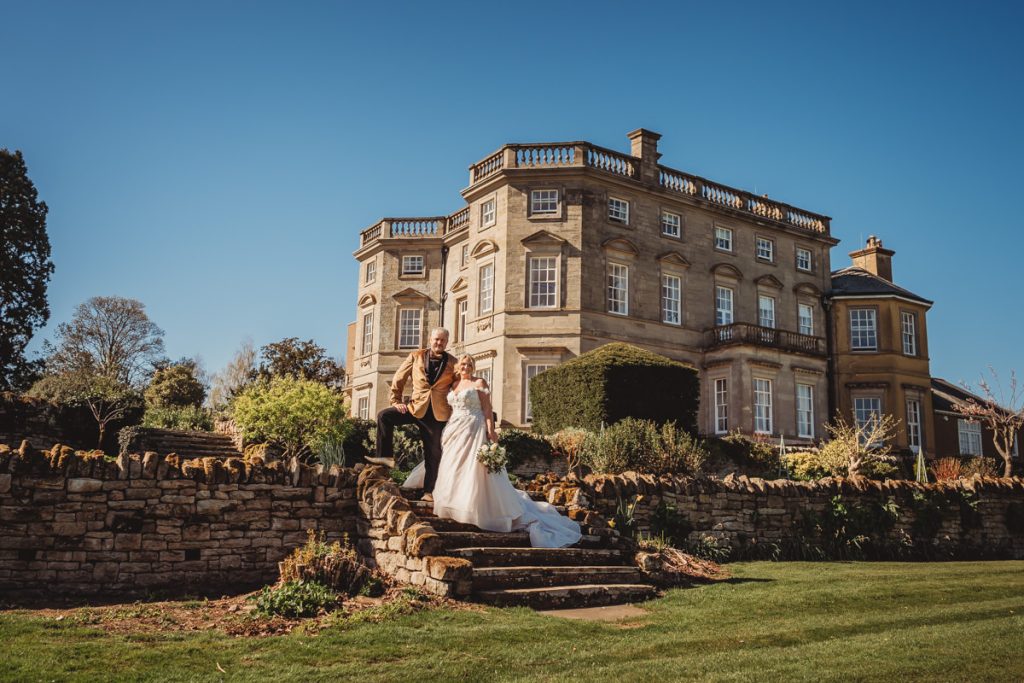 Couple posing outside stately home on wedding day at Bourton Hall by Tom Stenlake Photography