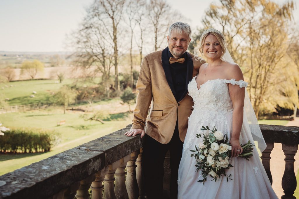 Couple on balcony with countryside backdrop, smiling at Bourton Hall by Tom Stenlake Photography