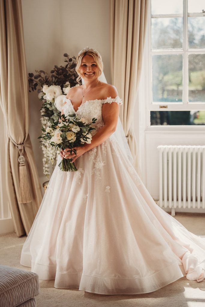 Bride smiling in elegant wedding gown with bouquet at Bourton Hall by Tom Stenlake Photography