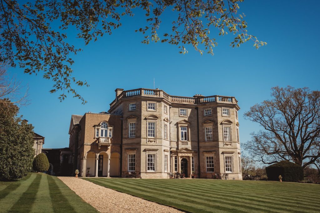 Historic mansion with manicured lawn and blue sky at Bourton Hall by Tom Stenlake Photography