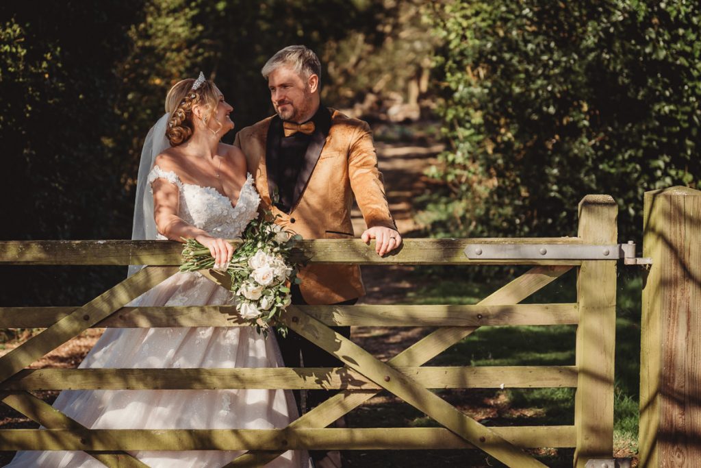 Bride and groom at a wooden gate outdoors at Bourton Hall by Tom Stenlake Photography