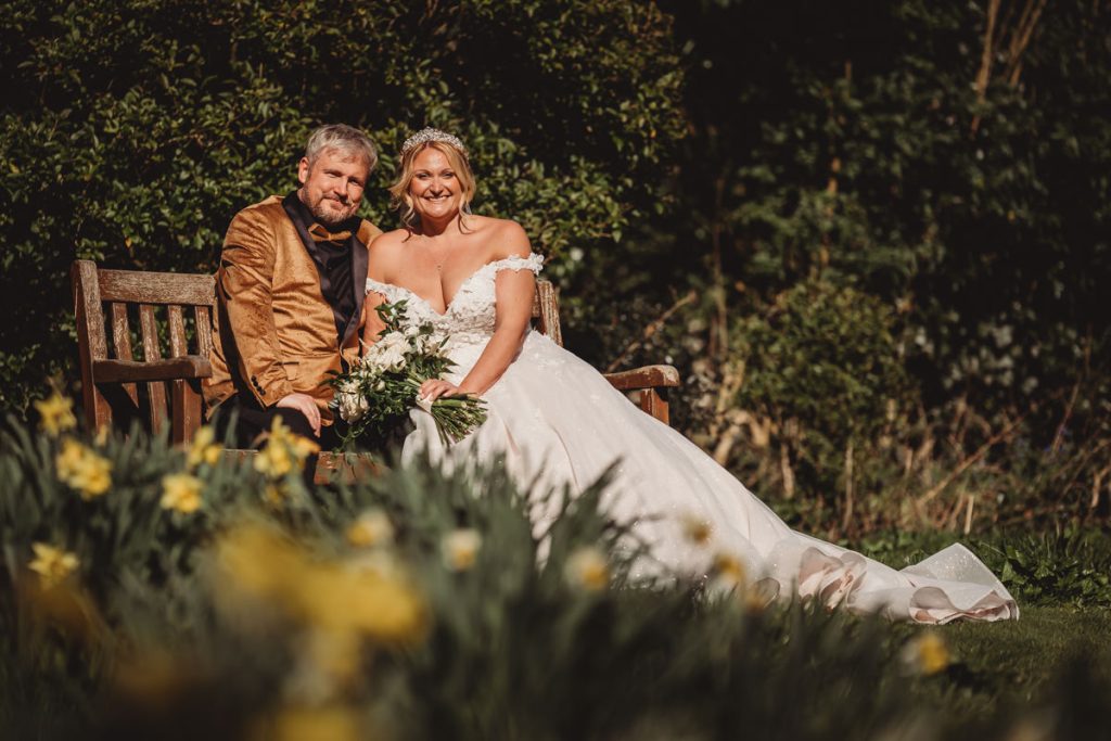 Bride and groom sitting on garden bench together at Bourton Hall by Tom Stenlake Photography