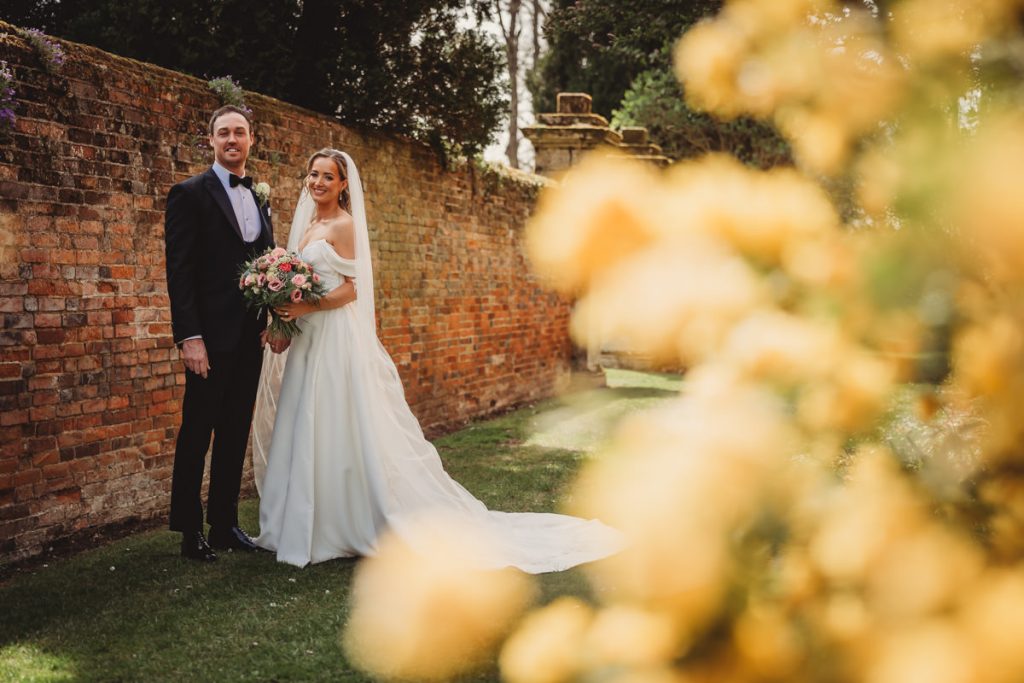Bride and groom beside brick wall, wedding day at Chicheley Hall