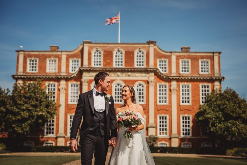Happy couple outside elegant manor house on wedding day at Chicheley Hall