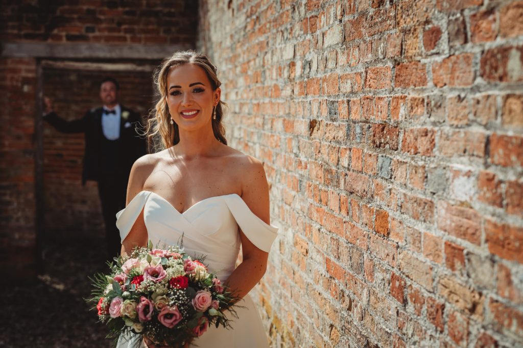 Bride holding bouquet by a brick wall at Chicheley Hall