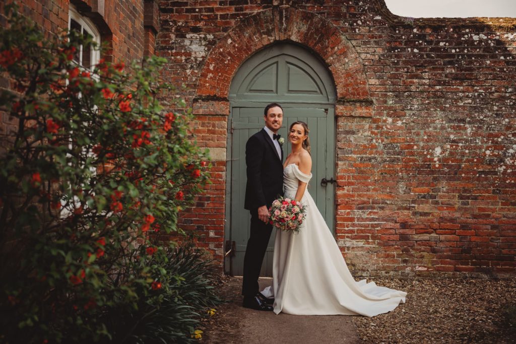 Bride and groom posing by rustic brick wall at Chicheley Hall