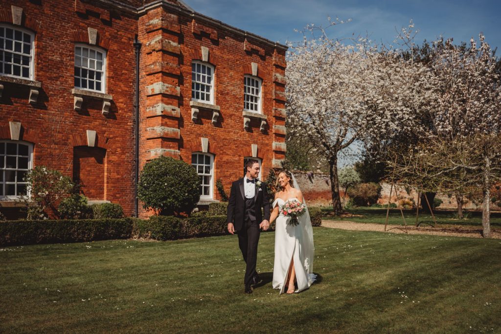 Bride and groom walking by brick building at Chicheley Hall