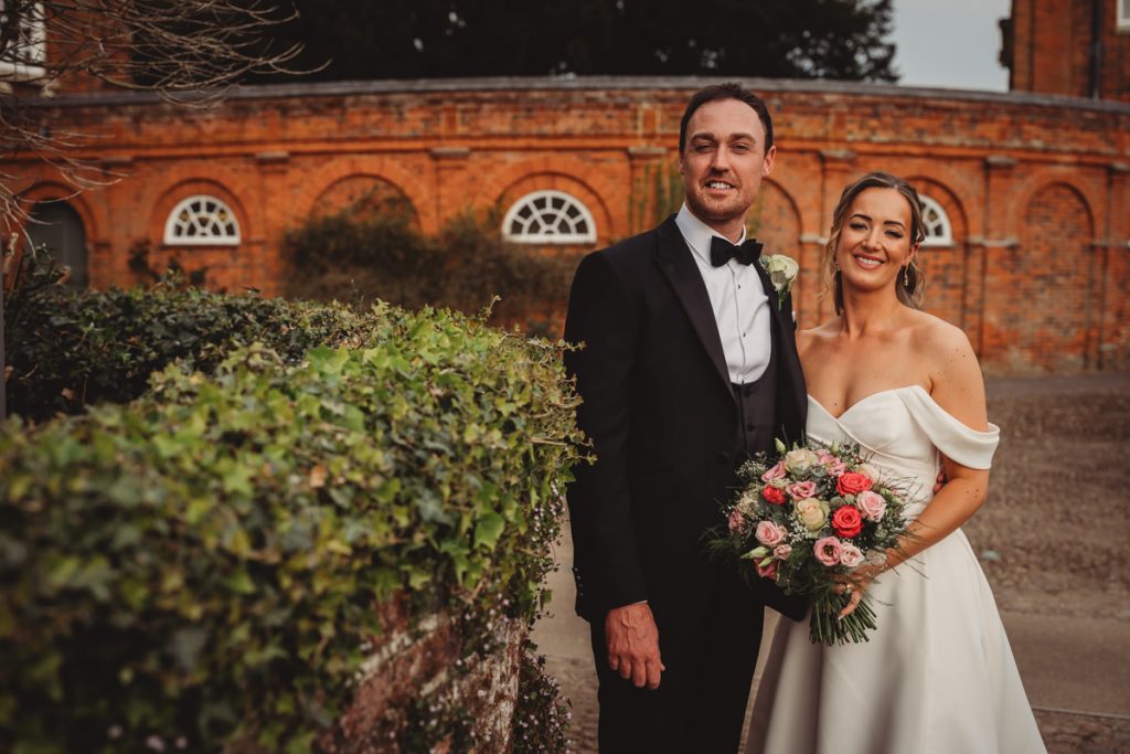 Bride and groom smiling in front of brick wall at Chicheley Hall