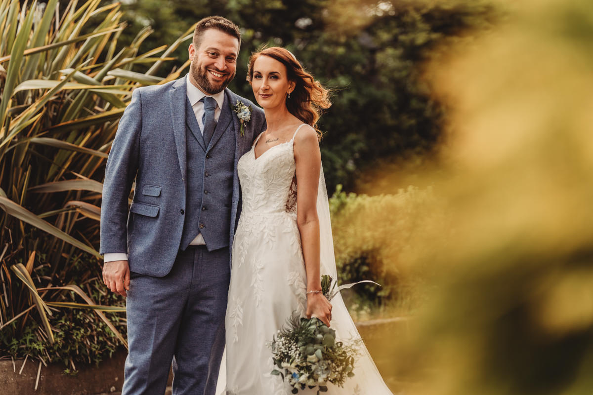 Smiling couple in wedding attire outdoors.