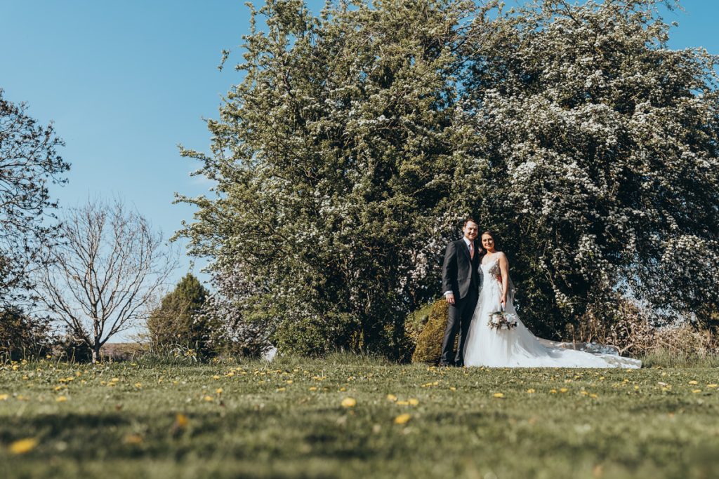 Newlyweds pose under flowering tree in garden at Huntsmill Farm