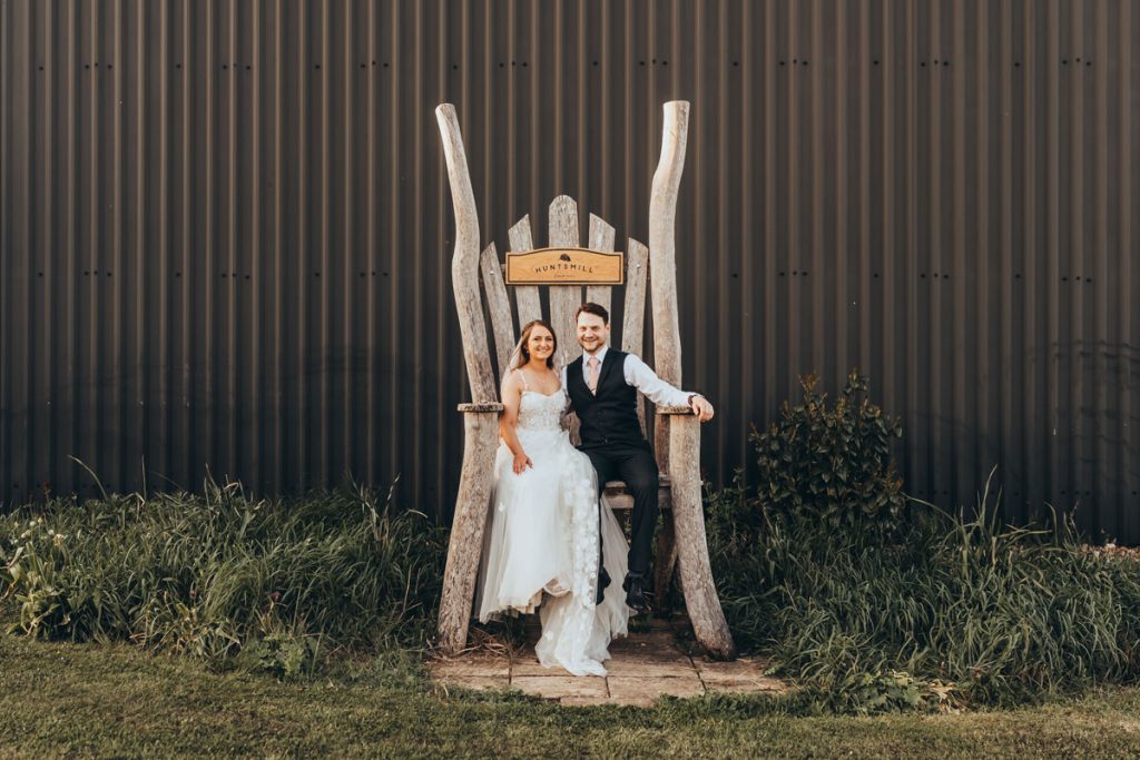 Couple sitting on a large wooden chair outside at Huntsmill Farm