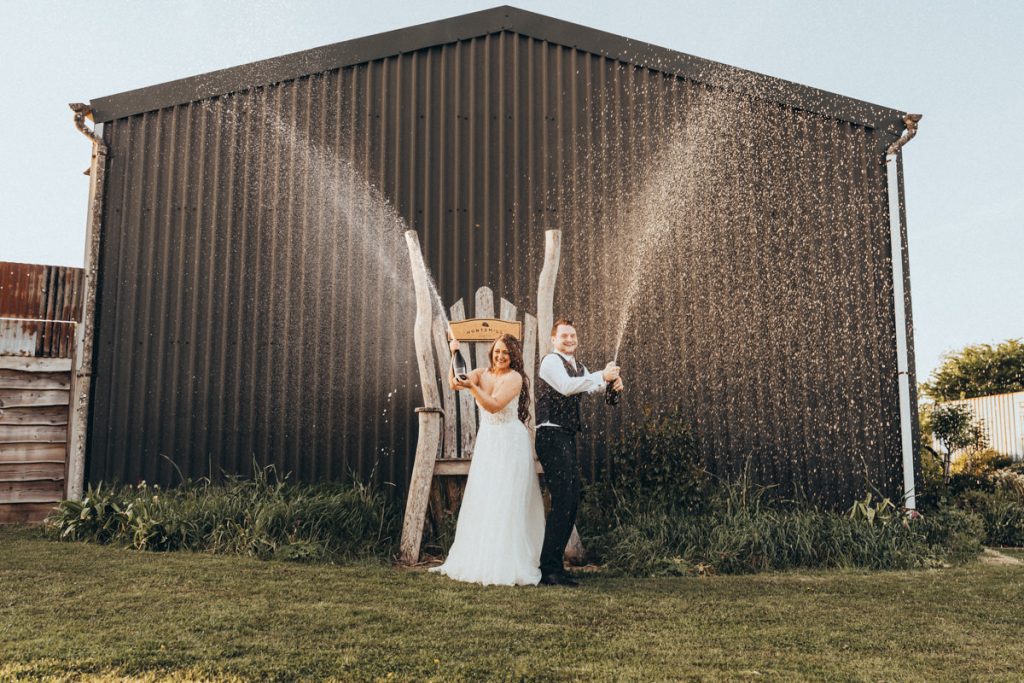 Couple celebrating with champagne outside barn at Huntsmill Farm