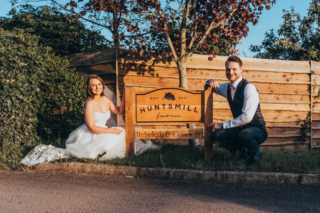 Bride and groom beside a Huntsmill Farm sign at Huntsmill Farm