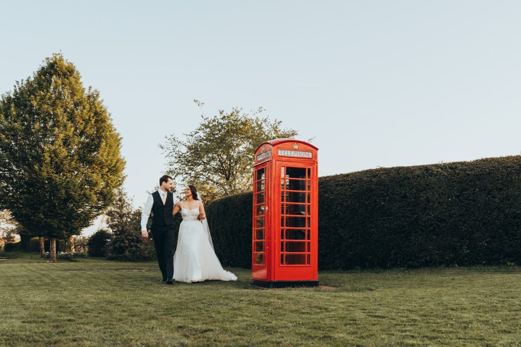 Wedding couple walking by red telephone box at Huntsmill Farm