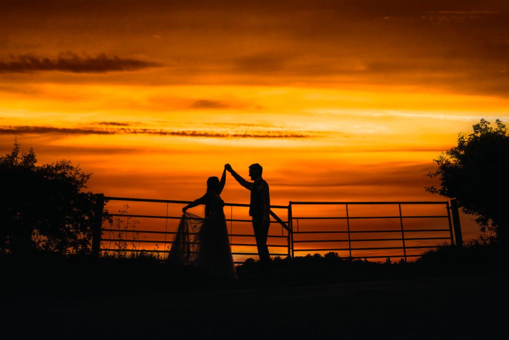 Silhouette couple dancing at sunset by the gate at Huntsmill Farm